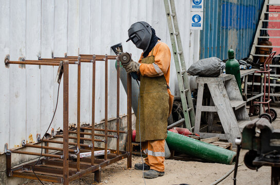 The worker is grinding the welding place to apply electrical ark welding. It is industrial area - surfer repairing center - where metal works takes place to repair metal elements