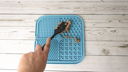 Person applying wet food to a dog to stimulate brain activity by licking a mat designed for that purpose, a lick mat or lick pad © Peludis