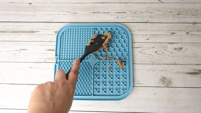 Person applying wet food to a dog to stimulate brain activity by licking a mat designed for that purpose, a lick mat or lick pad