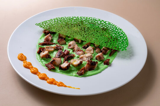 Fine dining octopus dish with green Parmentier cream, crispy herb tuile and gourmet restaurant presentation.