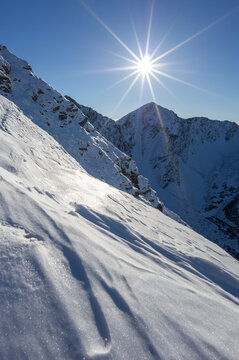 View of Volovec in Western Tatras with snow-covered slopes under a bright sun with a starburst effect and clear blue sky Witow, Lesser Poland Voivodeship, Poland.