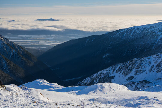View of Volovec in Western Tatras with snow-covered mountain peaks, a deep valley, and a thick sea of clouds under a clear blue sky Witow, Lesser Poland Voivode, Poland.