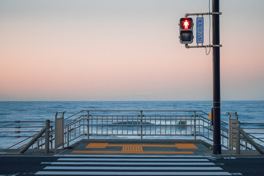 View of a pedestrian crossing and red traffic light overlooking the ocean at Shichirigahama Beach under a soft sunset sky in Kamakura, Kanagawa, Japan.