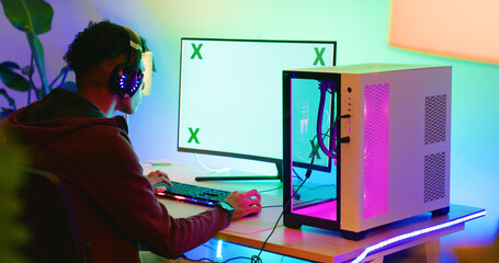 Gamer, computer screen and teen with headphones in home for esports competition, action and back. Headset, boy and gaming monitor for gameplay challenge, online match or mockup space with neon light © peopleimages.com