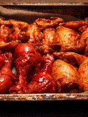 Naklejka premium Uncooked marinated chicken selection of drumsticks, thighs and wings in spicy hot buffalo sauce in a metal cooking container on a wooden table surface. Summer season popular food for barbeque.