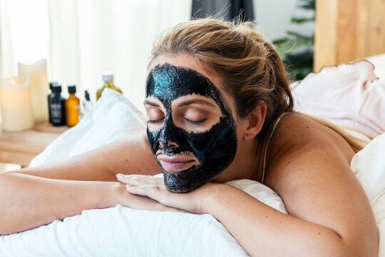 Beautiful young woman with clay facial mask in beauty spa. Detox ritual.