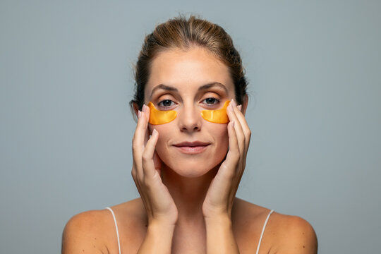 Pretty woman with orange hydrogel under eye patch on isolated grey background