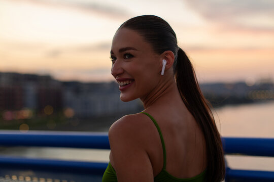 Smiling woman in blue sports bra and wireless earbuds standing on bridge