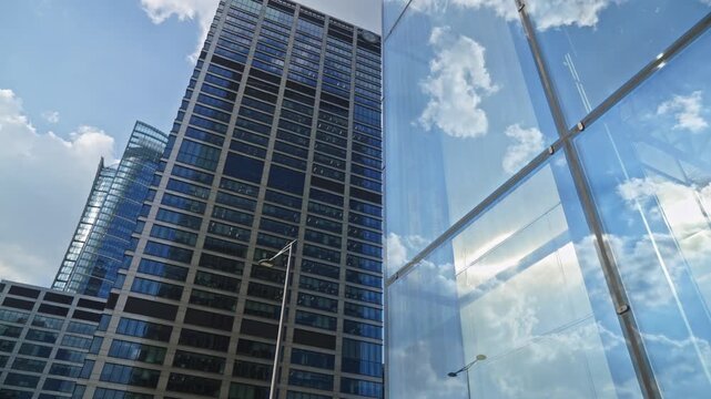 Smooth dolly style camera movement near modern office towers and business buildings with blue sky reflections, showing financial district architecture and success