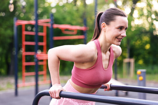 Athletic woman exercising on parallel bars at outdoor gym