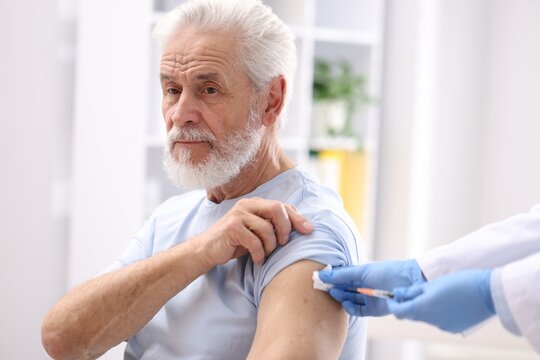 Doctor in medical gloves pressing patient's injection site after vaccination with cotton wool in clinic, closeup
