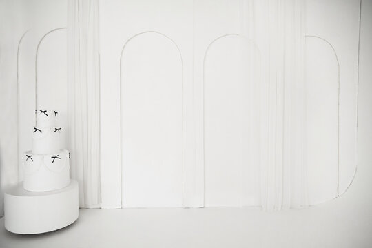 Elegant white three-tiered cake with black bows in minimalist arch interior