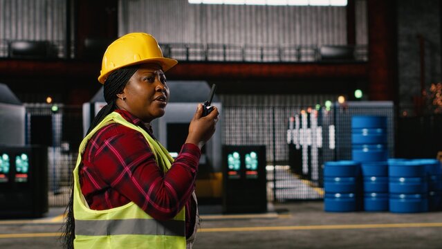 Woman engineer, portable walkie-talkie, speak with colleagues, walking across warehouse, worker supervising machinery hall workstations, Wireless radio transceiver near sparks from welding.