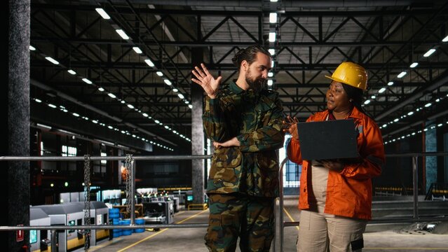 Engineering specialist and armed forces officer inspect heavy machinery in large-scale facility, Wartime economy ensures military support and industrialization powering national defense mission.