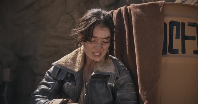 Injured woman in sci-fi world resting near barrel and throwing ball for off-screen animal