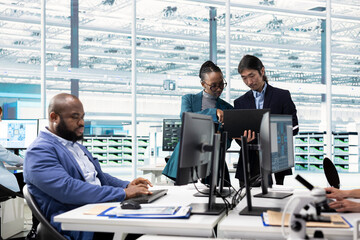 Engineers examining microchip circuit design on computer monitors using specialized software,...