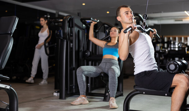 Determined young guy training on lat pull down exercise machine in fitness hall