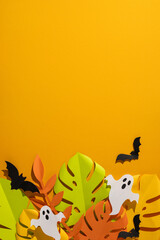 Obraz premium Tropical vertical Halloween paper leaves and ghost decorations with bats on bright orange background