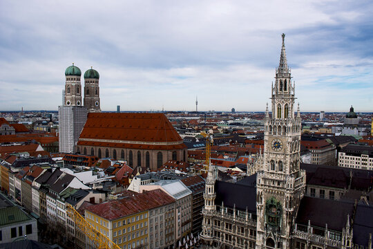 View of the historic Frauenkirche cathedral and the ornate New Town Hall tower overlooking the city skyline under a cloudy sky in Munich, Bavaria, Germany.