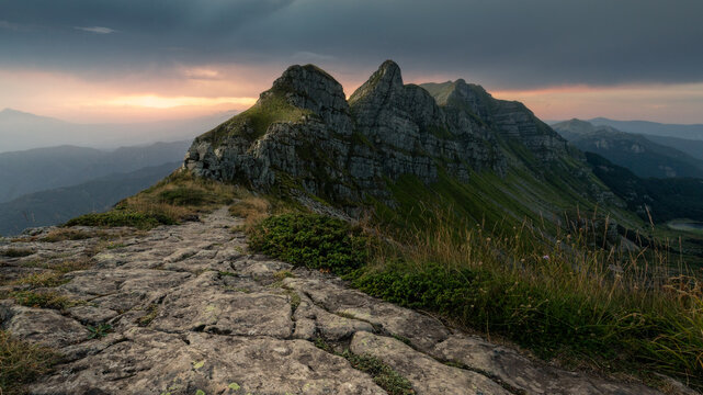 View of the rugged rocky peaks of the Apennine Mountains with a stone path along a ridge under a dramatic sunset sky Pievepelago, Emilia-Romagna, Italy.