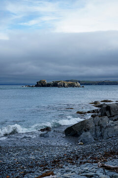 Atmospheric coastal view of Freshwater, Conception Bay, looking towards historic Carbonear Island, Newfoundland and Labrador, Canada. Moody day at a stony pebble beach with rugged Atlantic shores
