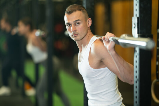 Determined young guy working out with weight rod in gym during training session