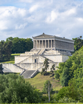 View of the Walhalla memorial with its neoclassical columns on a lush green hillside under a cloudy sky in Donaustauf, Bayern, Germany.