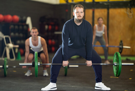 Focused motivated young bearded man performing barbell deadlift to increase strength and stability of back, glutes and hamstrings during intense cross training at gym