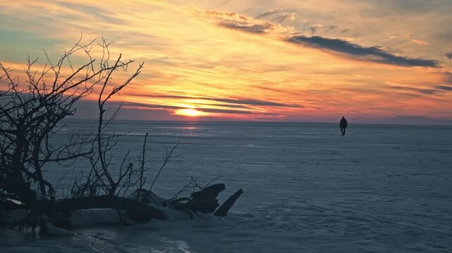 Lonely man walking thick ice frozen Dnieper River. Spectacular colorful winter sunset, dramatic golden hour light reflection snow covered surface. Cinematic peaceful majestic winter landscape Ukraine.