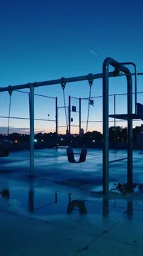 Vertical video: Swaying empty swing seat in light breeze on wet rooftop, camera panning skyline