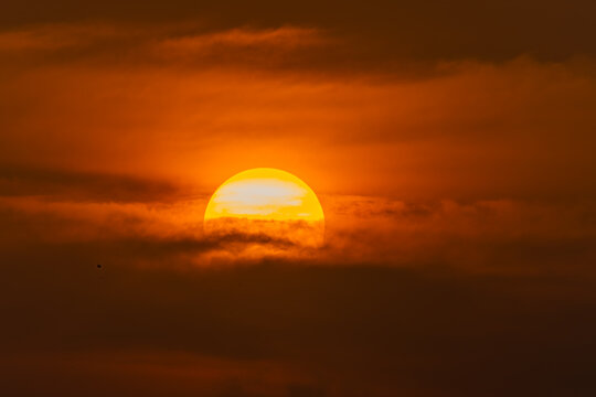 View of a large glowing sun setting behind dark atmospheric clouds in an orange sky Male, Male, Maldives.
