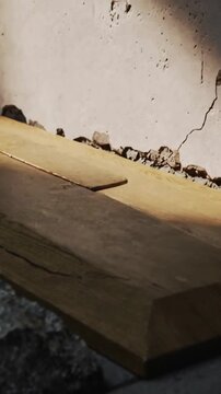 Vertical video: Panning camera showing wooden plank on rough concrete, cracked wall, sawdust rising