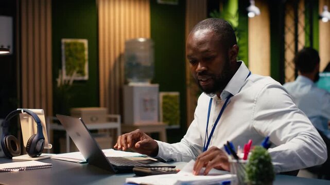 African american manager analyzes company data for accounting task, reviewing administrative business intel and building action plan. Employee at desk working late, project management.