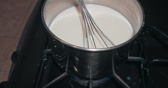 Whisker in creamy white sauce in a pot over a lit gas burner