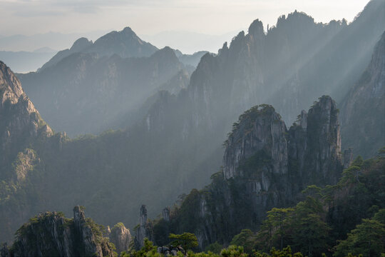 View of the jagged granite peaks and ancient pine trees of the Huangshan Mountains under dramatic light rays in Huangshan City, Anhui, China.