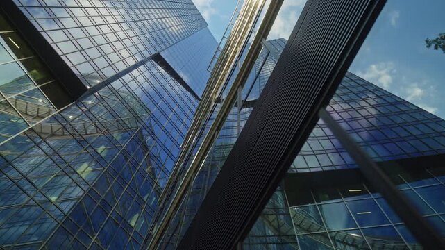 Low angle smooth cinematic dolly movement between modern glass skyscrapers in business district, corporate architecture, urban growth, financial success and contemporary city development