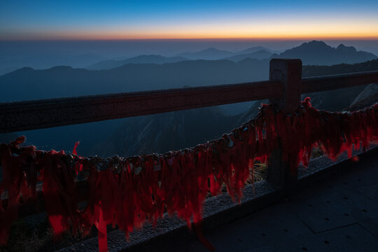 View of red prayer ribbons and locks tied to a stone railing overlooking the silhouette of mountain peaks at dawn in Huangshan City, Anhui, China.
