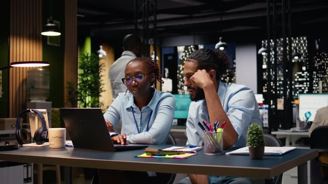 Diverse manager and assistant reading inbox emails on laptop late at night. Team analyzing data on notebook and interpreting statistical information, ensuring accounting assignments.
