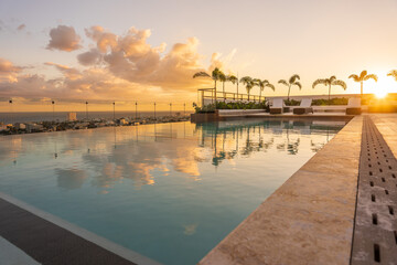 Obraz premium Luxury infinity pool reflecting a beautiful golden sunset in the Caribbean