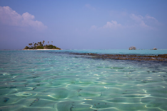 View of an uninhabited tropical island with palm trees across crystal clear turquoise water and a coral reef in Vashafaru, Thiladhunmathee Uthur, Maldives.