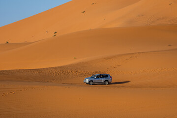 Obraz premium Off-road SUV crossing golden Sahara dunes near Merzouga, Morocco