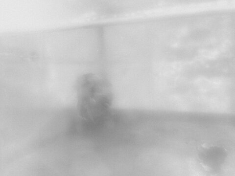 Abstract grey background captured through a heavily steamed or foggy glass window shows blurry, distorted shapes of trees and buildings outside under a dramatic overcast sky.