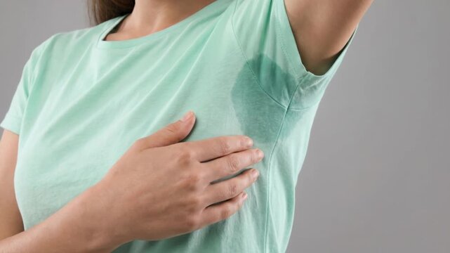 Unrecognizable young woman showing large wet sweat stain under armpit on light green t-shirt. Concept of hyperhidrosis, body odor problem, and personal hygiene