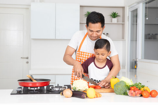 Father Teaching Young Son How to Cut Vegetables in Kitchen