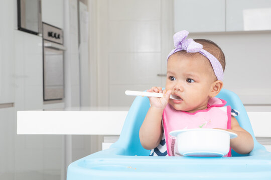 Adorable Baby Girl Learning to Eat with Spoon in High Chair
