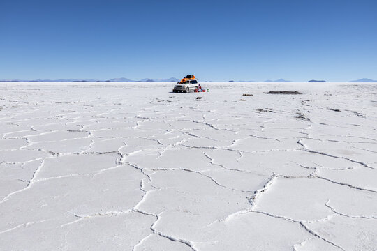 View of the Uyuni Salt Flat with its hexagonal salt crust patterns and an off-road vehicle under a clear blue sky in Potosi Department, Bolivia.