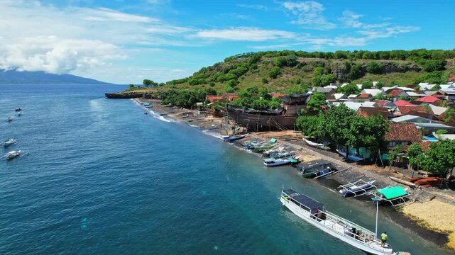 Aerial drone footage of Sangiang Wera local fishermen village in east Sumbawa island, Indonesia, with local wooden fishing boats, many Bajo traditional houses, and a big phinisi boat in construction
