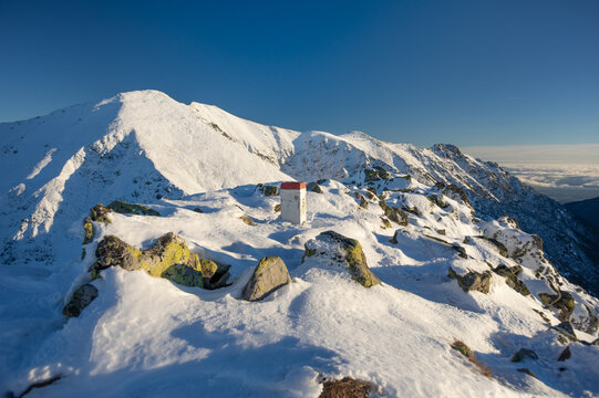 View of Koncisty Vrch in Western Tatras with a snow-covered rocky peak and a white boundary marker under a clear blue sky Pribylina, Zilinsky kraj, Slovakia.