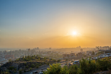 Obraz premium Sunset over Yerevan, Armenia with golden light shining across the city. The roads and cars below reflect the soft sunlight, creating a lively urban evening scene.