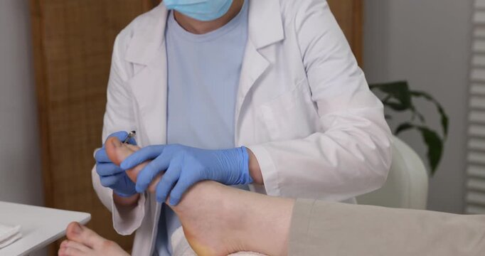 Podiatrist trimming patient's toenails with nail nippers in clinic, camera moving in